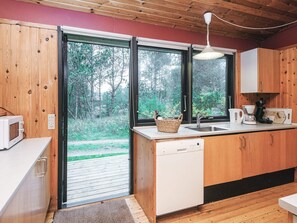 A compact kitchen with wooden cabinets, a white dishwasher, a microwave, a coffee maker, and a basket on the counter. - Charming Holiday Home in BlÃ¥vand with Hot Tub (Blavand)