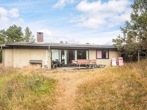 A single-story building with a covered patio area, a barbecue grill, and a table and chairs. - Charming Holiday Home in BlÃ¥vand with Hot Tub (Blavand)
