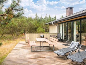 An outdoor deck with a wooden table and benches, a grill, and a glass-enclosed area with seating. - Charming Holiday Home in BlÃ¥vand with Hot Tub (Blavand)