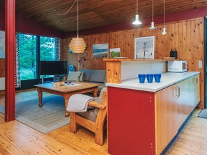 A cozy living area with a wooden floor, a sofa, a coffee table, and a TV. There is a kitchen area with a microwave and a counter. - Charming Holiday Home in BlÃ¥vand with Hot Tub (Blavand)