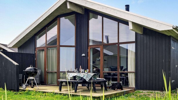 A modern house with large windows, a patio with a table and chairs, and a barbecue grill. - 8 Person Holiday Home in Ulfborg-by Traum (Ulfborg)
