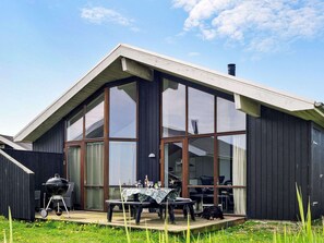 A modern house with large windows, a patio with a table and chairs, and a barbecue grill. - 8 Person Holiday Home in Ulfborg-by Traum (Ulfborg)