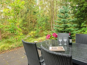 Uma mesa ao ar livre com cadeiras de vime, uma garrafa de vinho e um copo.