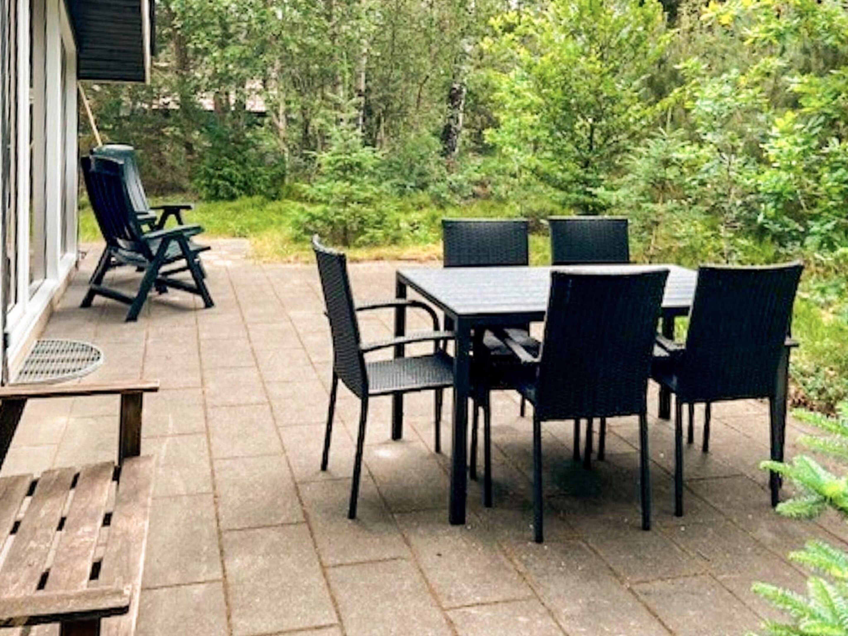 An outdoor patio with a table and chairs, surrounded by greenery.