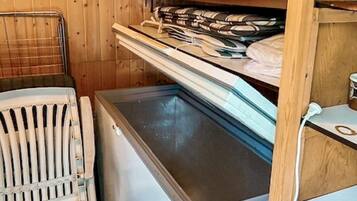 A compact room with a built-in ice chest, a radiator, and a shelf with folded towels.