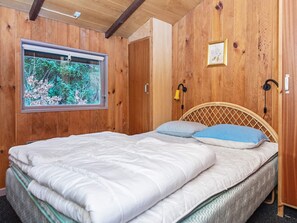 Ein Zimmer mit Holzwänden, einem Bett, einem Fenster mit Blick ins Grüne und einer Wandleuchte.