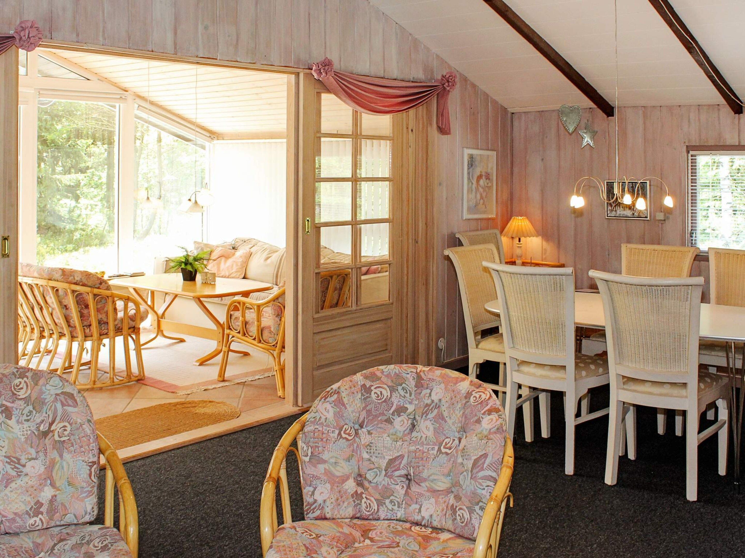 A cozy dining area with wicker chairs and a table, a separate seating area with a sofa, and a view through a glass door.