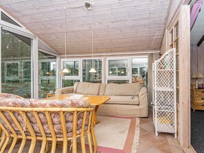 Um quarto aconchegante com teto de madeira, um sofá, uma mesa com cadeiras e janelas amplas.