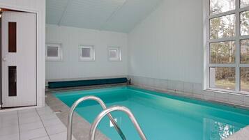 En swimmingpool med flisegulv, en metalstige og en dør til et andet rum.