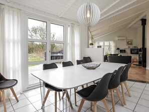 Un espace repas avec une table blanche et des chaises noires, de grandes fenêtres et un luminaire suspendu.