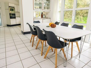 A modern kitchen with white cabinets, a built-in oven, and a dining area with a white table and black chairs.