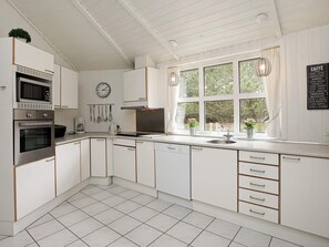 A modern kitchen with white cabinetry, stainless steel appliances, a clock, and a window with a view of greenery.