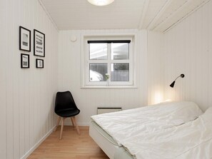 A bedroom with a bed, a chair, a window, and wall-mounted pictures.