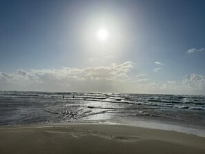 A beach with waves, a clear sky, and the sun shining.