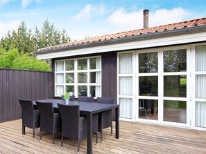 Une terrasse avec une table et des chaises, une clôture sombre et un bâtiment doté de grandes fenêtres et d’un toit recouvert de tuiles.