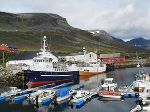 A harbor with boats docked, a red building, and a mountainous backdrop. - Holiday Home in Arnøyhamn (Skjervoy)