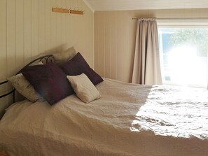 A bed with a patterned bedspread, a wooden headboard, and a window with curtains. - Holiday Home in Arnøyhamn (Skjervoy)