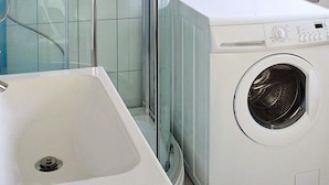 A modern bathroom with a white sink, a washing machine, and a glass shower enclosure. - Holiday Home in Arnøyhamn (Skjervoy)