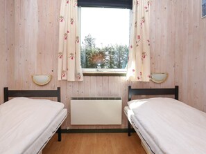 A room with two beds, a window with floral curtains, and a wall-mounted heater.