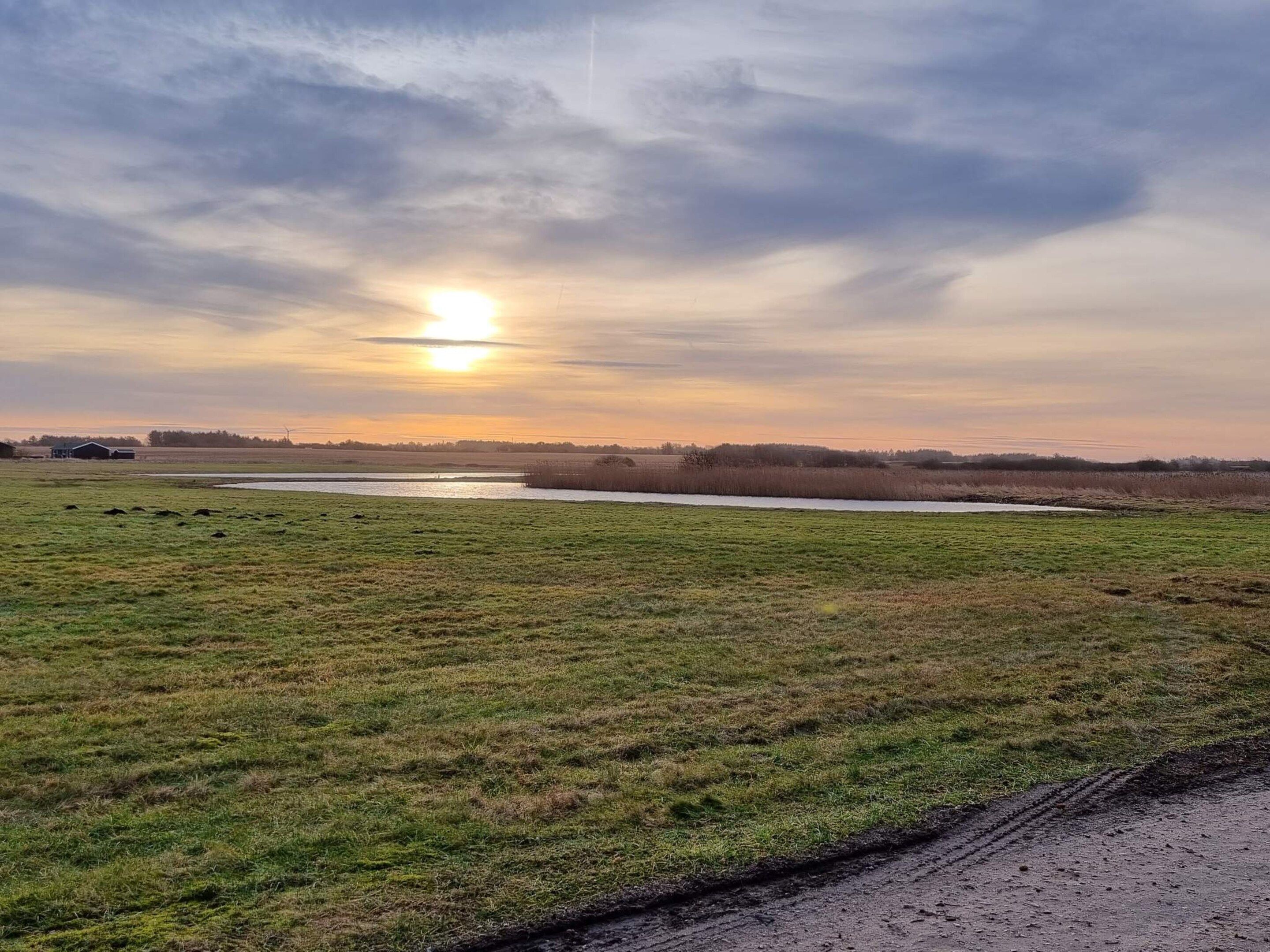 A rural landscape with a body of water, grassy fields, and a distant horizon.