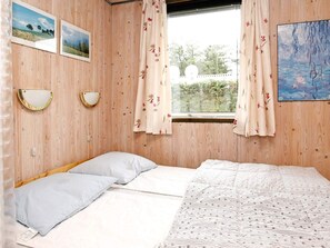 Une pièce comprenant un lit, deux lampes fixées au mur, une fenêtre avec des rideaux et deux tableaux encadrés accroch és au mur.