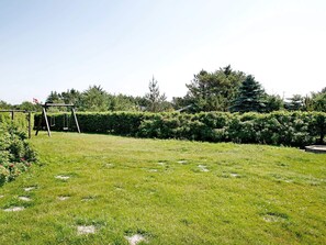 Un espace extérieur verdoyant avec une balançoire en bois et une haie.