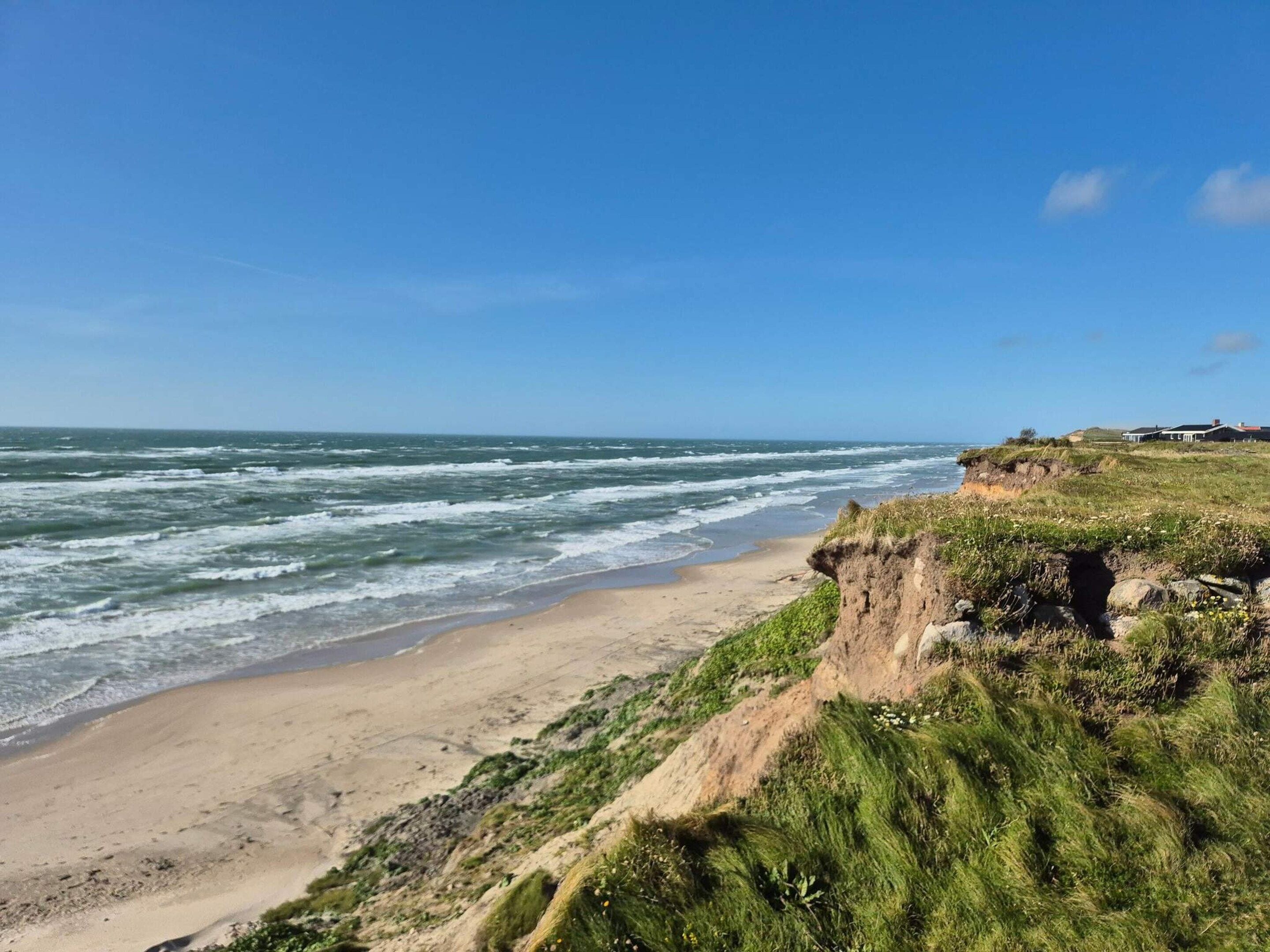 A coastal landscape with a sandy beach, grassy cliffs, and a clear blue sky.