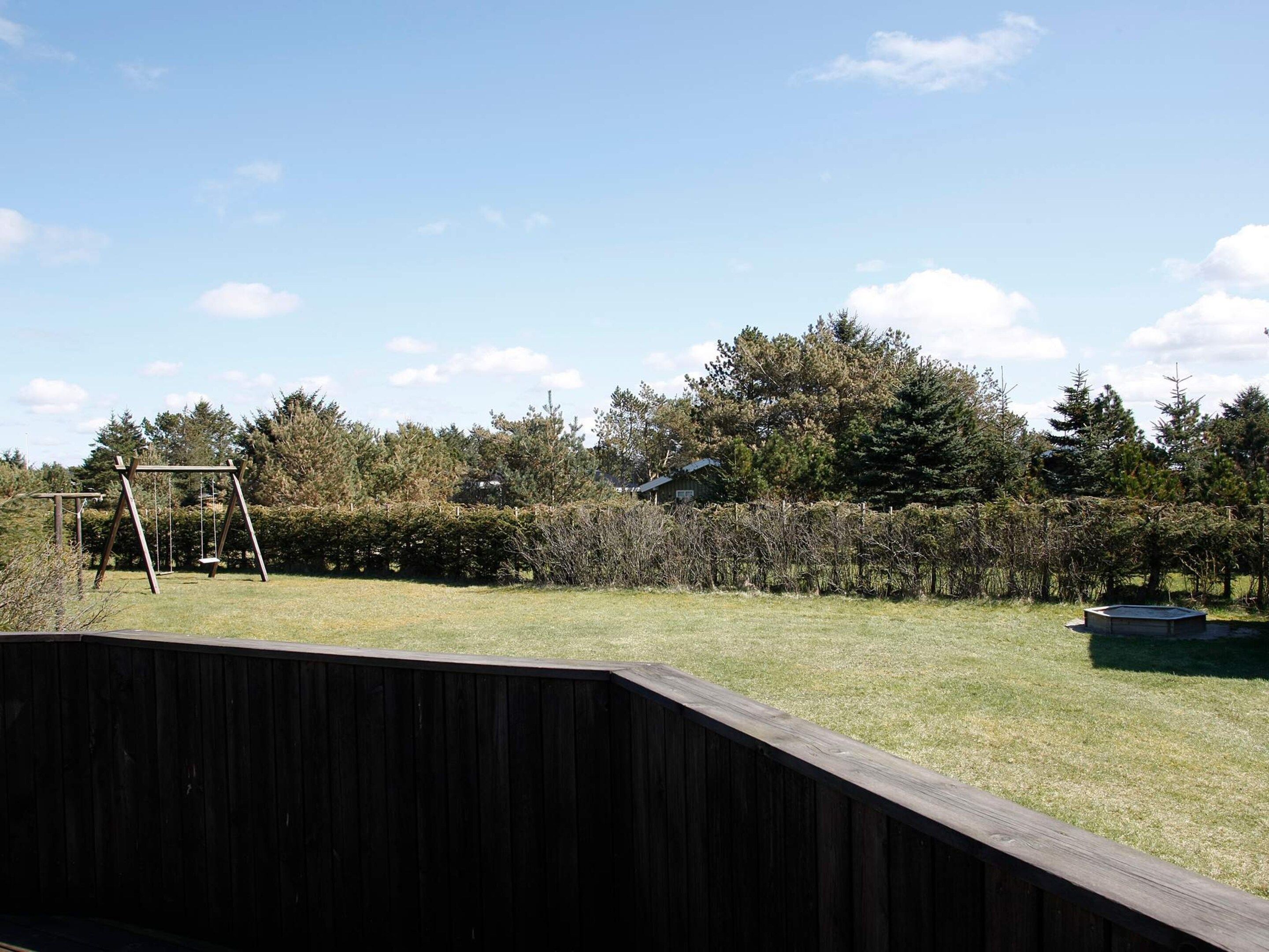 A backyard with a wooden swing set, a small pool, and a wooden deck.
