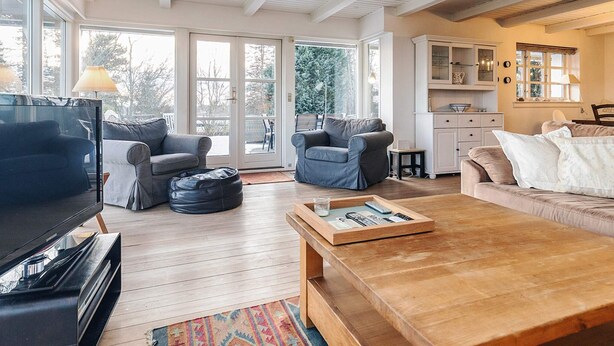 A spacious living room with a large TV, comfortable seating, a wooden coffee table, and a view through large windows. - 5 Person Holiday Home in Vejby-by Traum (Vejby)