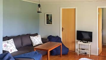 A living room with a sofa, a coffee table, a television on a stand, and a door leading to another room.