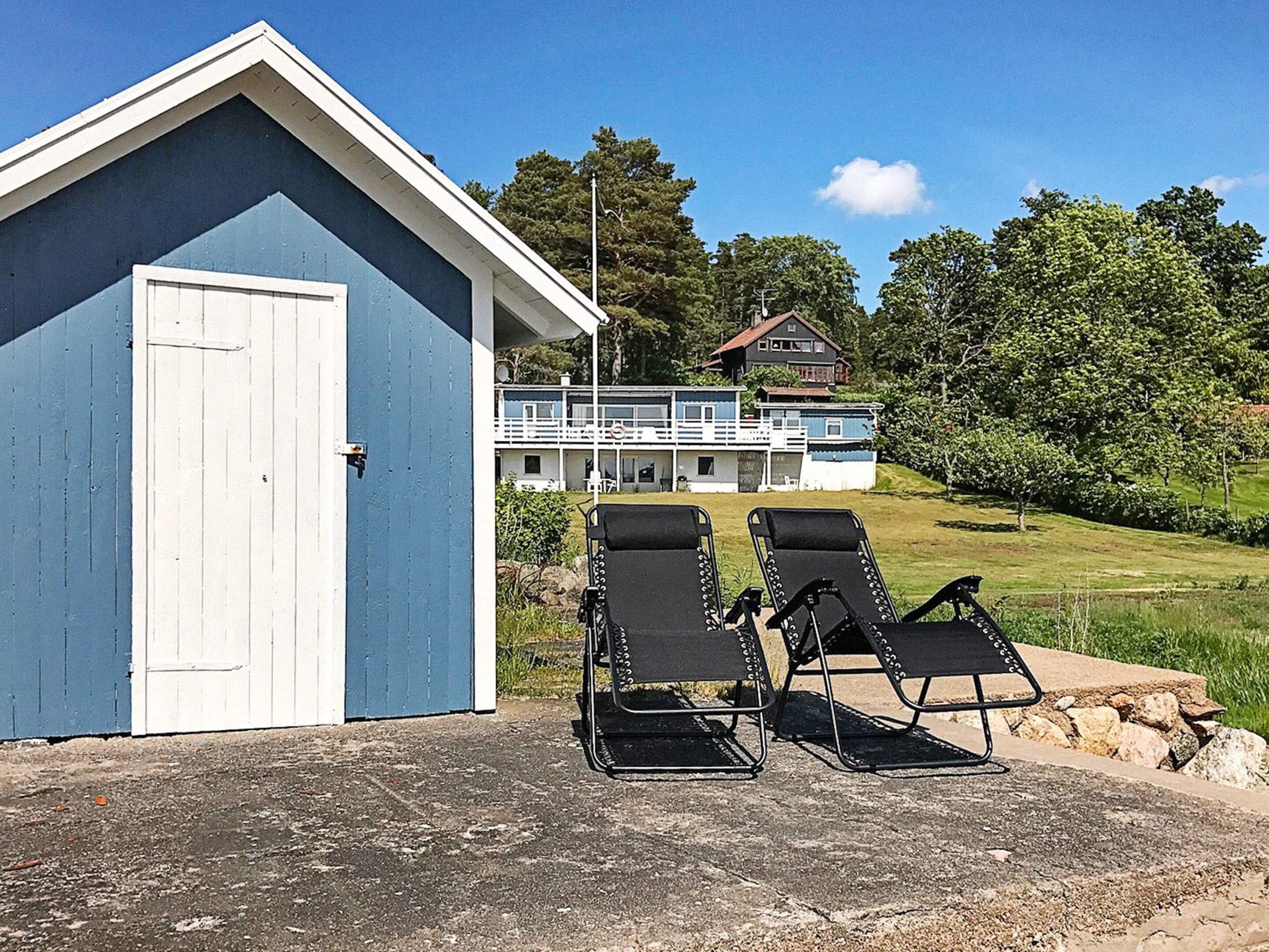 A building with a blue exterior, two black lounge chairs, and a view of a house with a balcony.
