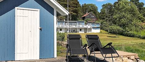 A building with a blue exterior, two black lounge chairs, and a view of a house with a balcony.