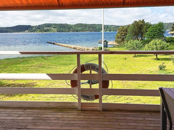 A wooden deck with a lifebuoy and a sign, overlooking a lake with a dock and a small building.