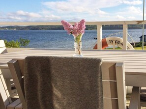 A deck with a table and chairs, a vase with flowers, and a view of a lake and distant land.