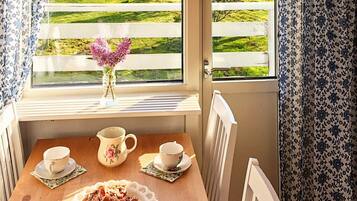 A room with a wooden table, two chairs, a window with a view of a green landscape, and a vase with flowers.