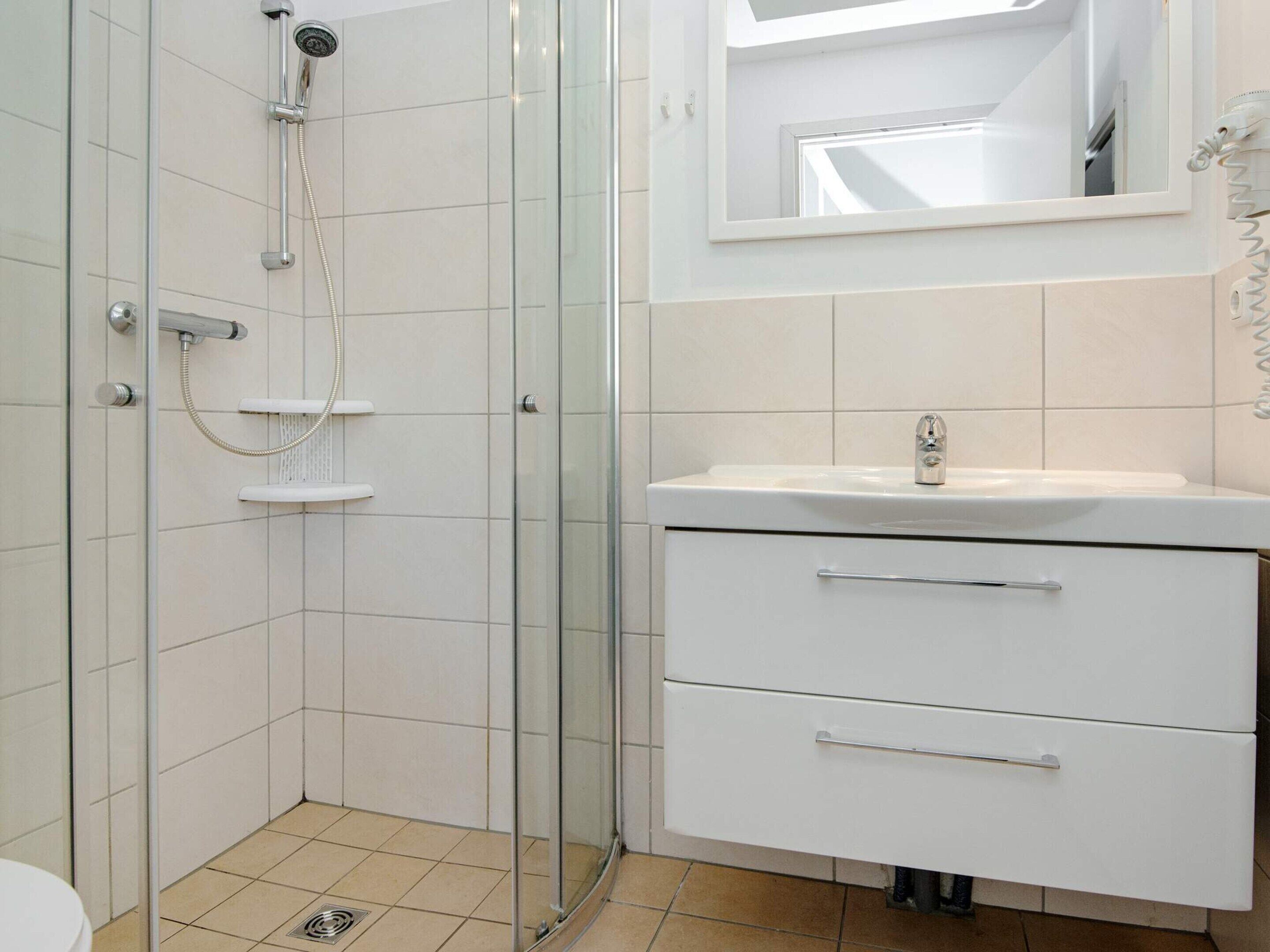 A bathroom with a glass-enclosed shower, a white sink with a mirror above it, and a white cabinet with drawers.