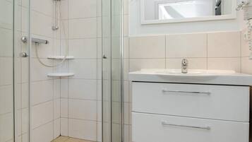 A bathroom with a glass-enclosed shower, a white sink with a mirror above it, and a white cabinet with drawers.