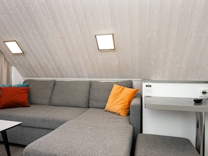 A modern interior with a grey sectional sofa, a small table, and a white countertop with a device. - Holiday Home in Wendtorf (Wendtorf)