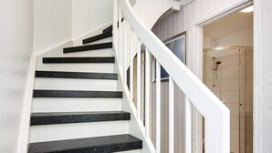 A staircase with white railings and black steps leading to a room with a shower.