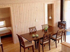 Un interior de madera con una mesa de comedor, sillas, un banco, una planta pequeña y un estufa de leña.