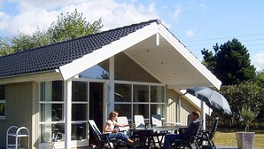 A covered outdoor seating area with a table and chairs, a covered patio, and a view of a house with large windows. - 5 Star Holiday Home in Dannemare (Dannemare)