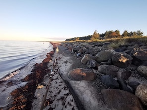 A rocky shoreline with a calm sea, a clear sky, and a distant view of land. - 5 Star Holiday Home in Dannemare (Dannemare)
