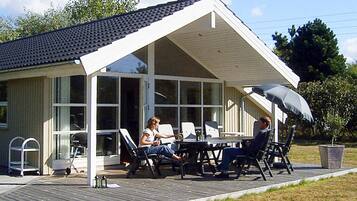 Een overdekt terras met een tafel en stoelen, een overdekte patio en uitzicht op een huis met grote ramen.