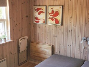 A room with wooden panel walls, a bed, a chair, and two wall-mounted artworks. - 5 Star Holiday Home in Dannemare (Dannemare)
