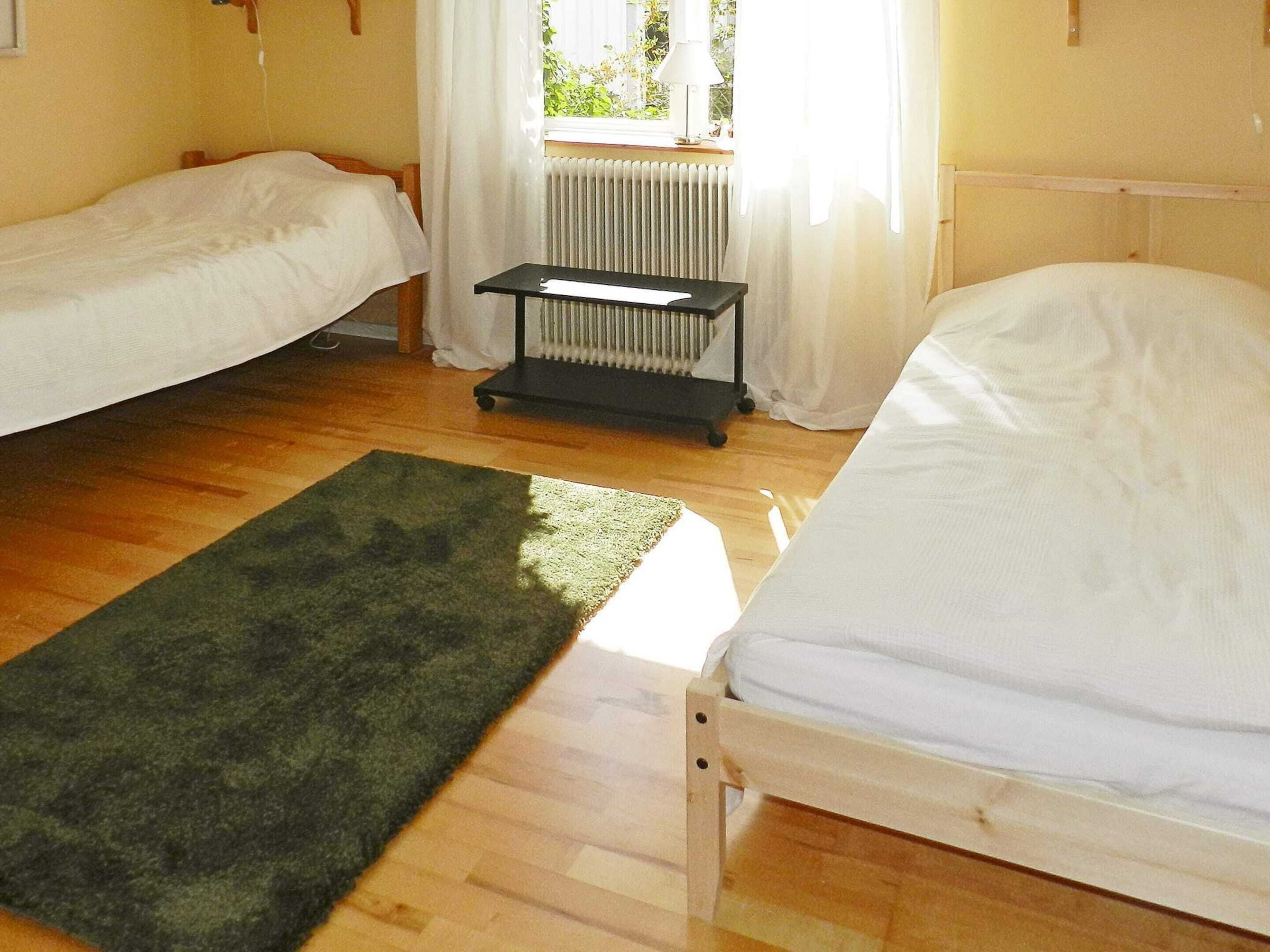 A room with two single beds, a radiator, a small table, and a green rug on a wooden floor.