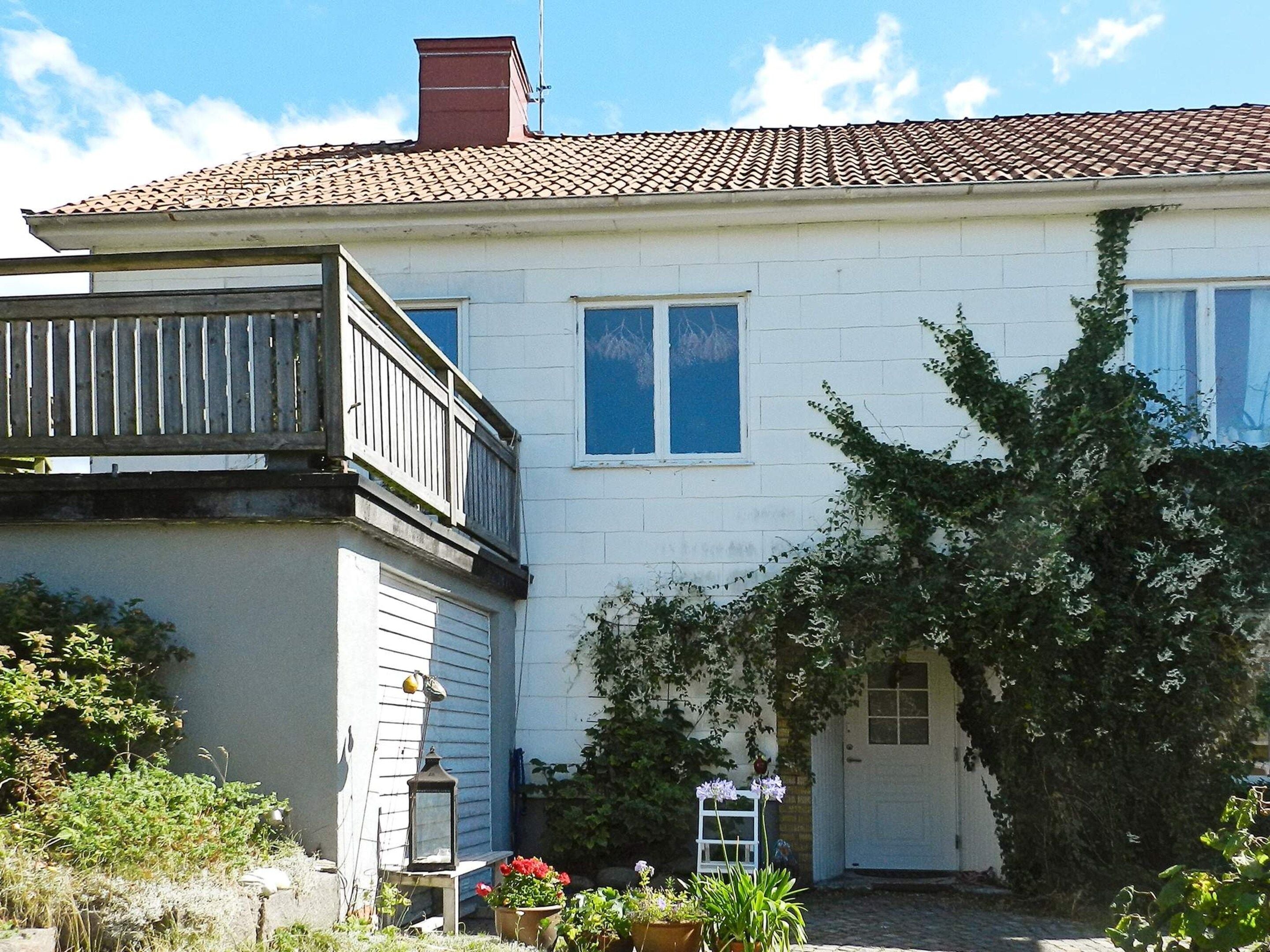 A two-story house with a balcony, a chimney, and a garden with potted plants and flowers.