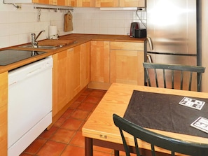 A compact kitchen with wooden cabinets, a dishwasher, a sink, and a table with chairs.