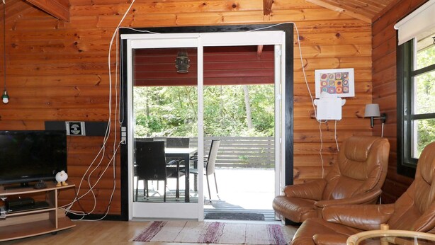 A cozy cabin interior with a wooden interior, a sliding glass door leading to an outdoor area, a television, and a leather chair. - Cheery Holiday Home in Hadsund near Sea (Hadsund)