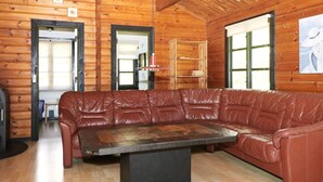 A log cabin interior with a leather couch, a central table, wooden floors, and a bookshelf. - Cheery Holiday Home in Hadsund near Sea (Hadsund)