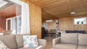 Un accogliente interno di una baita con pareti e soffitti in legno, una zona pranzo con tavolo e sedie, e una libreria.
